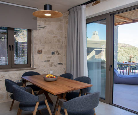Dining area with wooden table and chairs, stone walls and large balcony doors leading to outdoor seating