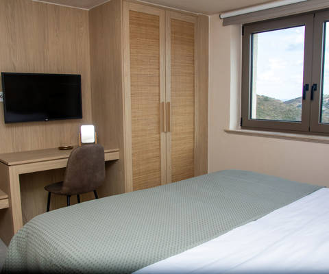 Bright bedroom with double bed, desk with chair, wardrobe, wall-mounted TV, and large window with a view