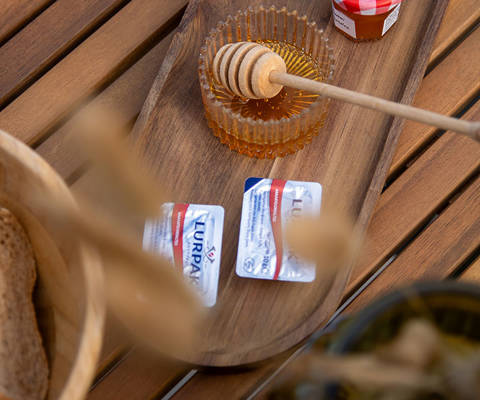 Close-up of a wooden tray with honey, jam jars and butter portions on a wooden table