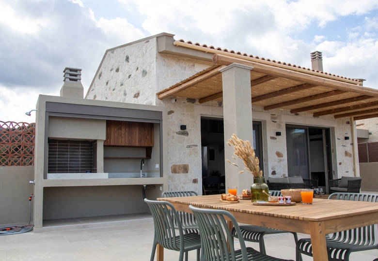Outdoor dining area with breakfast setup, barbecue station and view of a beautiful stone villa